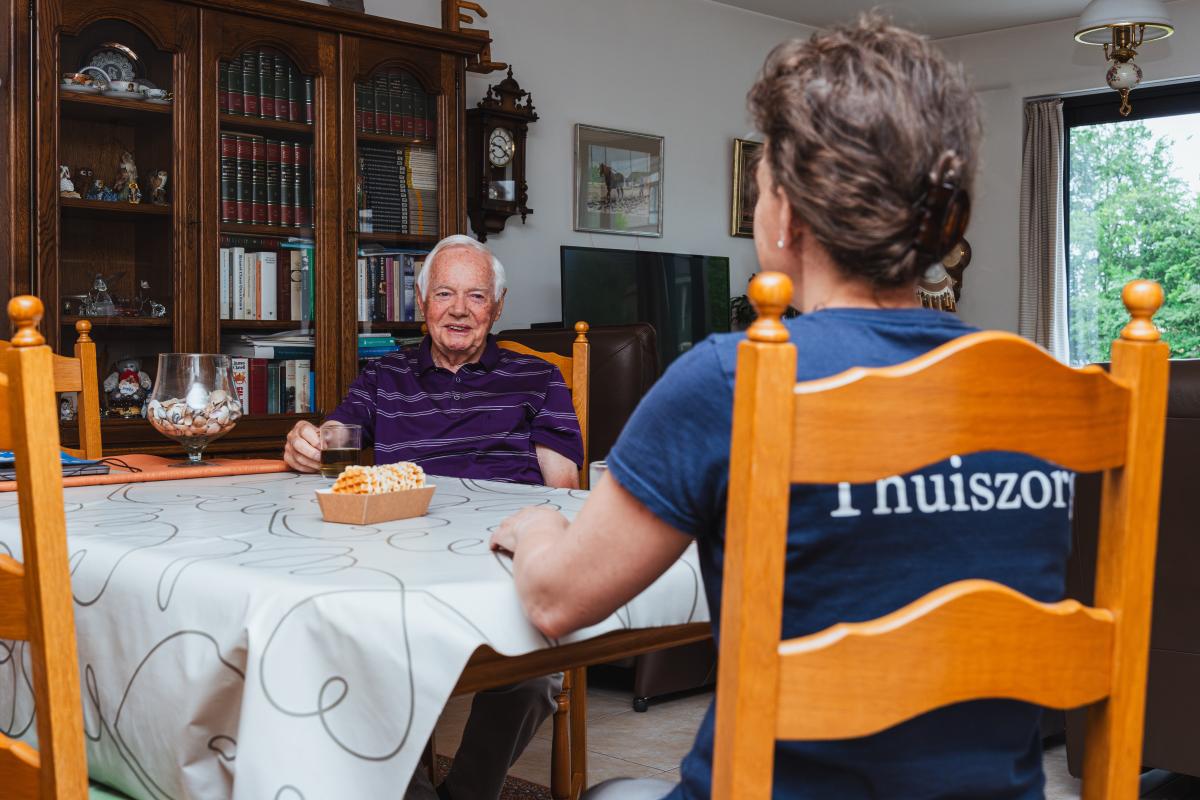 een verzorgende in de thuiszorg zit aan tafel bij een cliënt 