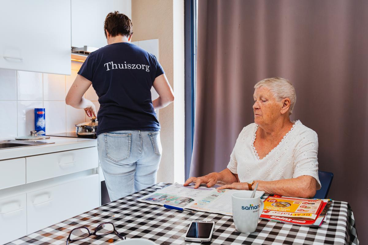 een verzorgende in de thuiszorg aan het fornuis bij een dame thuis