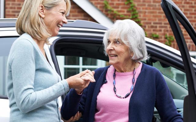 een vrouw helpt een oudere dame uit een auto