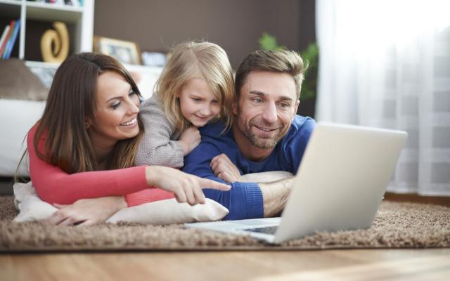 een gezin kijkt glimlachend naar een laptopscherm