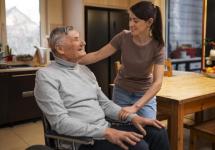 een oudere man in een rolstoel en een vrouwelijke mantelzorger