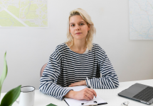 een vrouw zittend aan een bureau met pen, papier en enkele notitieboekjes